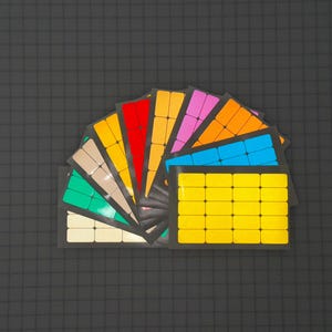 May include: A fan-shaped arrangement of colorful adhesive labels, each with a different color and pattern. The labels are arranged in a rainbow pattern, with red, orange, yellow, green, blue, and purple labels. The labels are all rectangular and have a smooth, glossy finish.