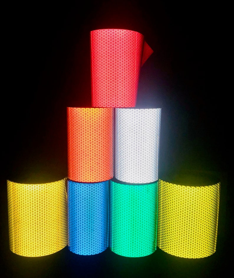 May include: A stack of six rolls of reflective tape in different colors: red, orange, white, blue, green, and yellow. The tape has a diamond pattern.