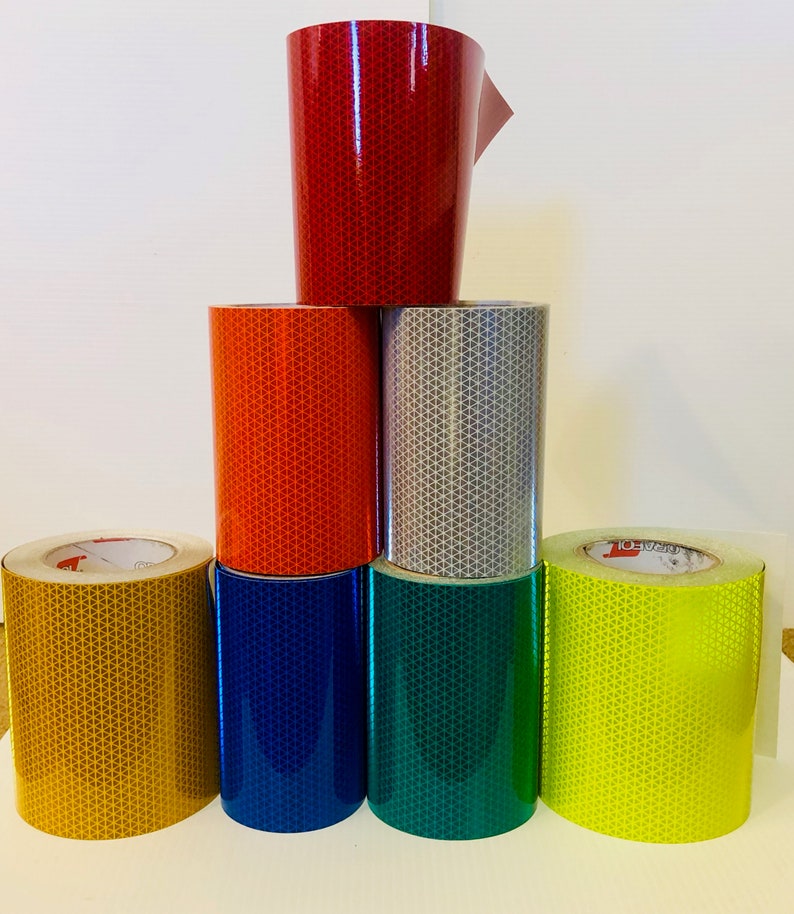 May include: A stack of seven rolls of reflective tape in various colors, including red, orange, silver, yellow, gold, blue, and green. The tape is designed for safety and visibility.