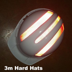 May include: White hard hat with three reflective orange and yellow strips on the side. The hard hat is designed for safety and visibility.