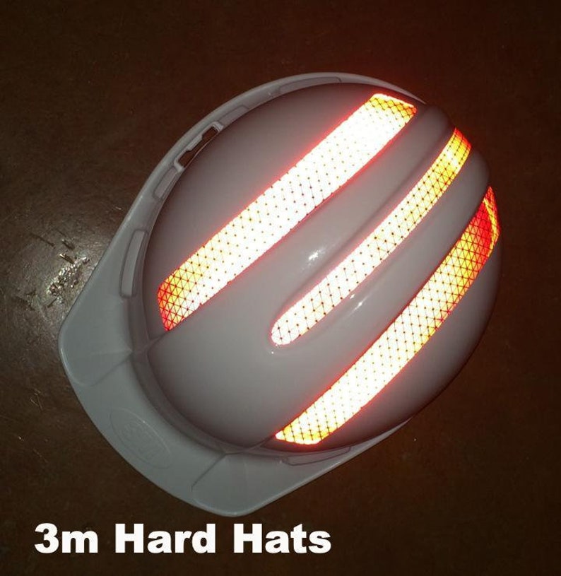 May include: White hard hat with three reflective orange and yellow strips on the side. The hard hat is designed for safety and visibility.