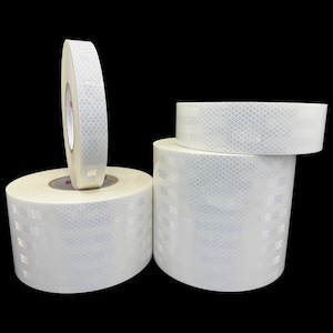 May include: Three rolls of white reflective tape with a diamond pattern. The tape is used for safety and visibility.