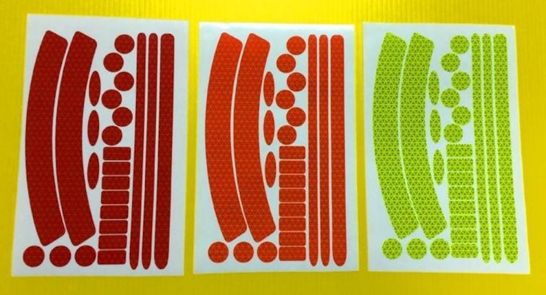 May include: Three sheets of reflective bike stickers. The stickers are in red, orange, and green. Each sheet has a variety of shapes and sizes of stickers, including circles, rectangles, and curved lines.