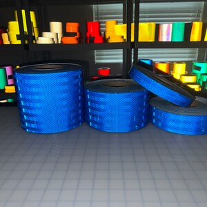 Puede incluir: Cuatro rollos de cinta reflectante azul, con un patr&oacute;n de diamante, est&aacute;n apilados sobre una superficie gris. La cinta se utiliza para la seguridad y la visibilidad.