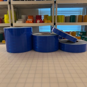 Puede incluir: Cuatro rollos de cinta reflectante azul. La cinta est&aacute; sobre una superficie de rejilla blanca.