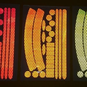 May include: Three sheets of reflective bike stickers in red, orange, and yellow. Each sheet contains a variety of shapes and sizes of stickers, including circles, triangles, and curved lines.