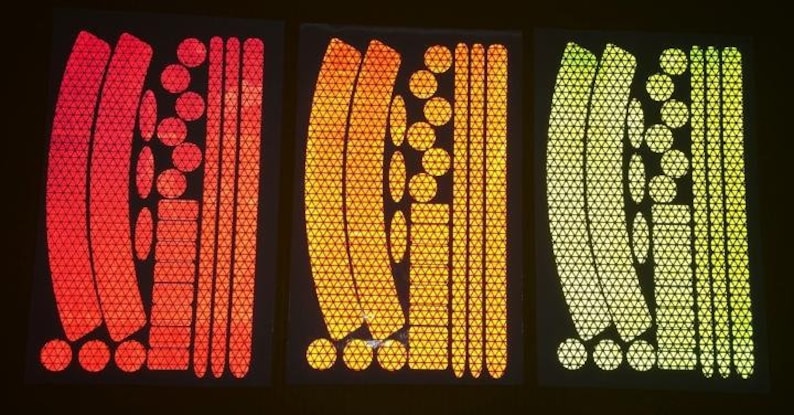 May include: Three sheets of reflective bike stickers in red, orange, and yellow. Each sheet contains a variety of shapes and sizes of stickers, including circles, triangles, and curved lines.