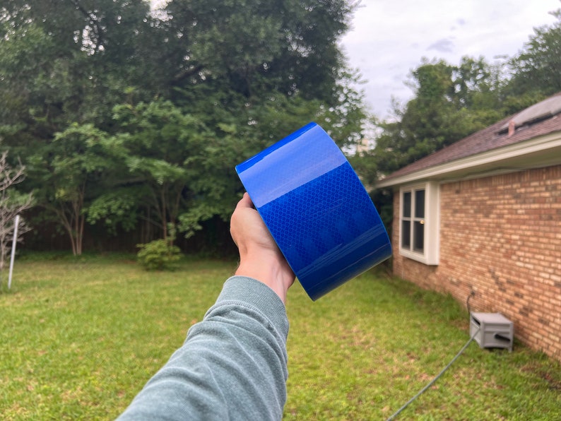 Puede incluir: Un rollo de cinta reflectante azul con un patr&oacute;n de diamante. La cinta se sostiene en una mano.