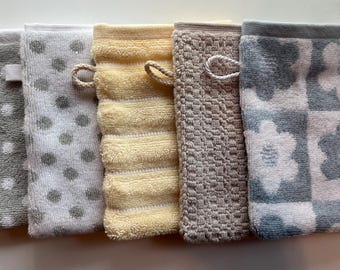 May include: A collection of six rectangular washcloths in various colors and patterns. The washcloths include gray with white polka dots, yellow with horizontal stripes, and gray with a floral pattern. Each washcloth has a loop for hanging.