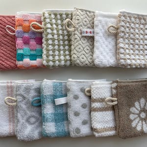 May include: A collection of twelve rectangular zippered pouches made of textured terry cloth fabric. Each pouch features a unique pattern, including stripes, checks, polka dots, and floral designs in various colors like pink, blue, beige, and white.