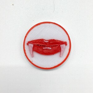 May include: A red and white 3D printed pin with a vampire mouth and fangs.