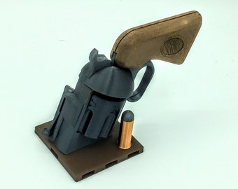 Può includere: Un modello di revolver stampato in 3D con un'impugnatura in legno marrone e un proiettile color rame. Il revolver è montato su una base marrone con una superficie testurizzata.