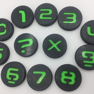 May include: A set of ten round black and green game pieces with numbers 0 through 9 and a question mark and an 'X' symbol.