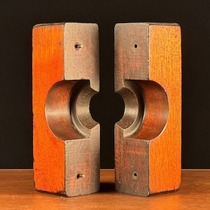 以下が含まれることがあります： 中央に円形の切り抜きのある木製のブロックが2つ。ブロックは赤褐色で、滑らかで磨かれた仕上げになっています。