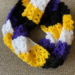 May include: A crocheted infinity scarf in yellow, black, white, and purple stripes. The scarf is made with a textured stitch.