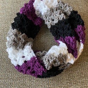 May include: A crocheted infinity scarf in purple, white, gray, and black. The scarf is made in a textured stitch and is a popular accessory for the fall and winter seasons.