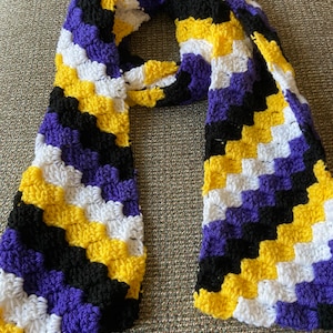 May include: A crocheted scarf in a chevron pattern with alternating stripes of purple, black, yellow, and white.
