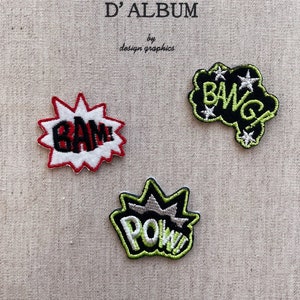 May include: Three embroidered comic book patches on a beige fabric. The patches feature the words "GAME", "BANG", and "POW" in bold lettering, with red, white, black, and green accents. The text "MON JOURNAL D'ALBUM" is at the top.