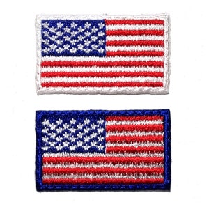 May include: Two embroidered patches of the American flag. The top patch has a white border, while the bottom patch has a blue border. Both feature a blue canton with white stars and red and white stripes.