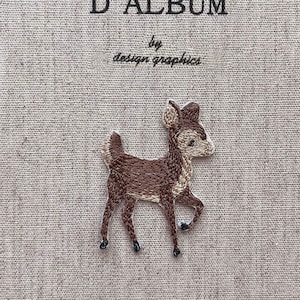May include: A beige journal cover with the text "MON JOURNAL D'ALBUM" and "by design graphics" embroidered in black. A brown deer embroidery is on the cover.