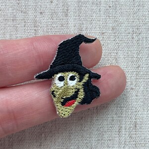 May include: Embroidered patch featuring a witch's face with a black hat, green skin, and a red mouth. The patch is small and detailed, perfect for adding to clothing or accessories. Ideal for Halloween or fantasy-themed projects.