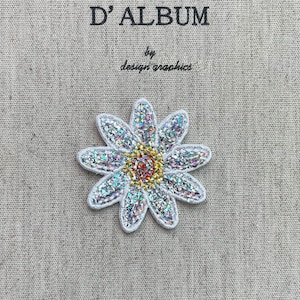 Op de afbeelding: Een sprankelende madeliefjespatch met een witte rand, iriserende bloemblaadjes en een goud-oranje centrum. De patch staat op een beige stof met de tekst "MON JOURNAL D'ALBUM" en "by design graphics".