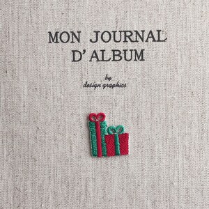 Op de afbeelding: Een beige stoffen tijdschriftomslag met de tekst "MON JOURNAL D'ALBUM" en "by design graphics" in het zwart. Twee geborduurde geschenkdozen, rood met groene strepen, staan in de rechter benedenhoek.