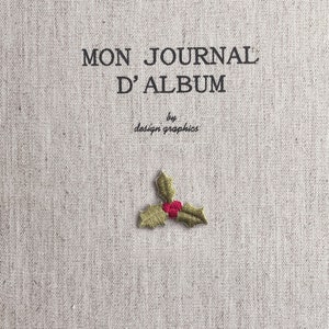 Puede incluir: Una portada de diario de lino beige con el texto "MON JOURNAL D'ALBUM" y "by design graphics" en negro. Una pequeña ramita de acebo bordada con bayas rojas está centrada en la parte inferior.