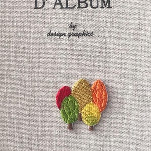 Könnte beinhalten: Ein beiger Tagebuchumschlag mit dem Text "MON JOURNAL D'ALBUM" und "by design graphics" in Schwarz. Ein farbenfrohes gesticktes Design stilisierter Bäume in Rot, Grün, Gelb und Orange befindet sich auf dem Umschlag.