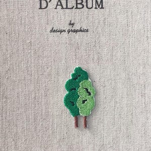 May include: A beige journal cover with the French text "MON JOURNAL D'ALBUM" and "by design graphics" in black. A small embroidered tree in shades of green and brown is on the cover.