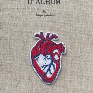 May include: A fabric patch featuring a detailed anatomical heart design in red, white, and blue, with a white border. The patch is placed on a beige fabric background. The text "MON JOURNAL D'ALBUM" is at the top, with "by design graphics" below.