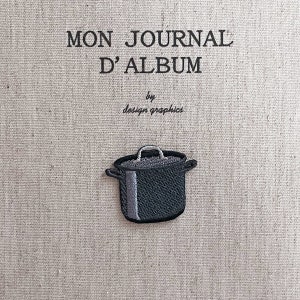 Puede incluir: Parche bordado con una olla negra con asa plateada y una franja gris. El parche está sobre un fondo de tela beige con el texto "MON JOURNAL D'ALBUM" y "by design graphics" en negro.