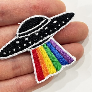Puede incluir: Parche bordado con un OVNI negro con detalles blancos y un rayo arcoíris. El OVNI tiene estrellas blancas y un borde blanco. Perfecto para personalizar ropa o accesorios.