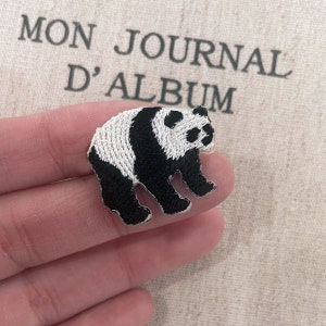 May include: Embroidered panda bear patch in black and white. The patch is in the shape of a panda bear standing on all fours. The background has the text "MON JOURNAL D'ALBUM".