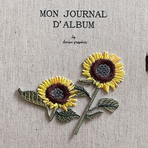 Peut inclure: Broderie de tournesols avec des pétales jaunes et des centres brun foncé sur un tissu beige. Le texte "MON JOURNAL D'ALBUM" et "by design graphics" sont au-dessus des fleurs. Les tournesols ont des tiges et des feuilles vertes.