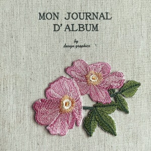 Può includere: Copertina di diario ricamata con la scritta "MON JOURNAL D'ALBUM" e "design graphics". Due fiori rosa ricamati con centri gialli e foglie verdi sono presenti sulla copertina.