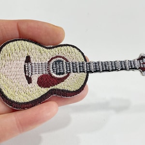 May include: Embroidered patch of an acoustic guitar. The patch features a cream-colored body with a dark red soundhole and a gray neck. The guitar is outlined in a dark brown thread.