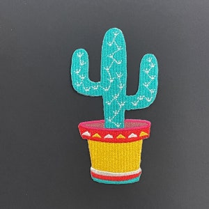 May include: An embroidered patch featuring a turquoise cactus with white stitched details, planted in a yellow pot with a red rim decorated with white and yellow triangles and a white horizontal stripe near the base of the pot.