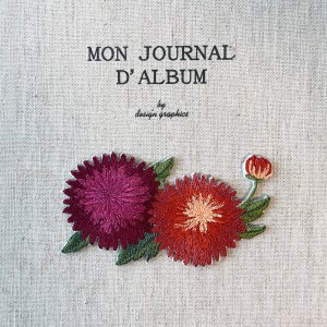 May include: A journal cover with the text "MON JOURNAL D'ALBUM" and "by design graphics". The cover features embroidered flowers in shades of red and purple with green leaves, set against a neutral linen background.