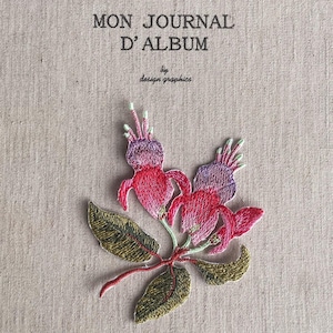 May include: Embroidered journal cover with the text "MON JOURNAL D'ALBUM" and "by design graphics." The cover features a detailed floral design with red, purple, and green embroidery on a beige background. The flowers are the focal point.
