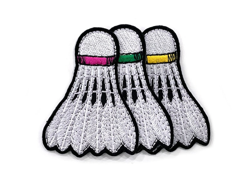 Peut inclure: &Eacute;cussons brod&eacute;s repr&eacute;sentant trois volants blancs avec des contours noirs. Chaque volant a une bande de couleur diff&eacute;rente : rose, vert et jaune. Pour les amateurs de sport.