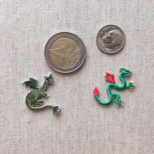 May include: Two embroidered dragon patches, one green with dark green wings and the other green with red accents. A US dime and a Euro coin are next to the patches, providing size reference.