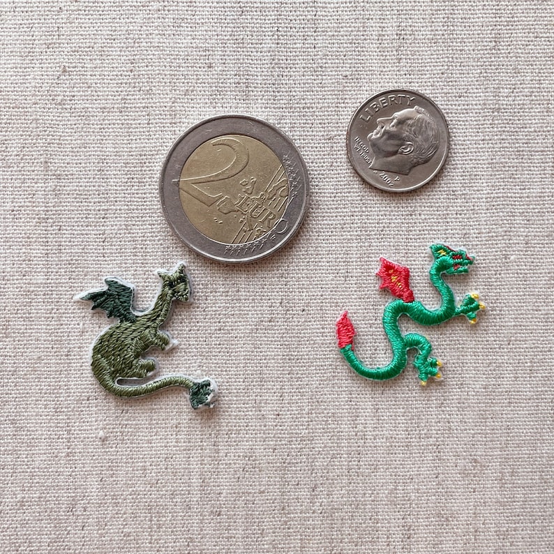 May include: Two embroidered dragon patches, one green with dark green wings and the other green with red accents. A US dime and a Euro coin are next to the patches, providing size reference.