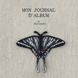 Może przedstawiać: Haftowana naszywka w kształcie motyla w kolorze czarno-białym, z czerwonymi i fioletowymi detalami, na tle beżowej tkaniny. U góry nadrukowano tekst "MON JOURNAL D'ALBUM" i "by design graphics".