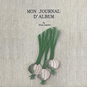 Op de afbeelding: Een beige tijdschriftomslag met de tekst "MON JOURNAL D'ALBUM" en "by design graphics" in zwart. De omslag heeft een geborduurd ontwerp van drie groene en witte uien.