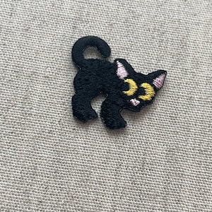 以下が含まれることがあります： 黄色い目とピンクのアクセントが付いた、黒い猫の刺繍パッチ。 猫は遊び心のあるポーズで、尻尾が丸まっています。 このパッチは、衣類、バッグ、その他の布製品に気まぐれなタッチを加えるのに最適です。