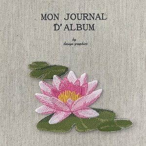 May include: A journal cover with the text "MON JOURNAL D'ALBUM" and "by design graphics". The cover features an embroidered pink and yellow water lily with green leaves on a beige fabric background.