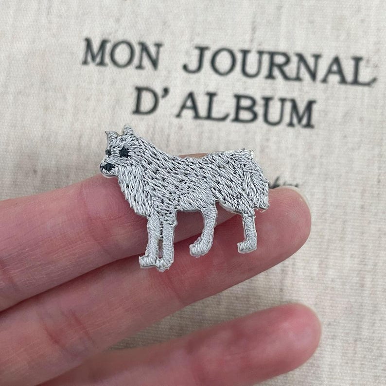 May include: Embroidered silver dog patch. The patch depicts a standing dog with detailed stitching. The background includes the text "MON JOURNAL D'ALBUM" in black.
