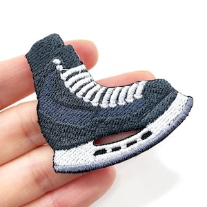 May include: Embroidered patch featuring a navy blue ice skate with white laces and a white blade. The patch is shaped like a single ice skate, with detailed stitching and a textured finish. Ideal for adding to clothing or accessories.