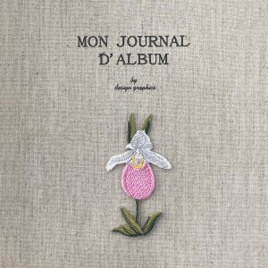 Puede incluir: Una portada de álbum de tela beige con texto bordado que dice "MON JOURNAL D'ALBUM" y "by design graphics". Una flor bordada rosa, blanca y verde está centrada en la portada. El álbum parece hecho a mano.